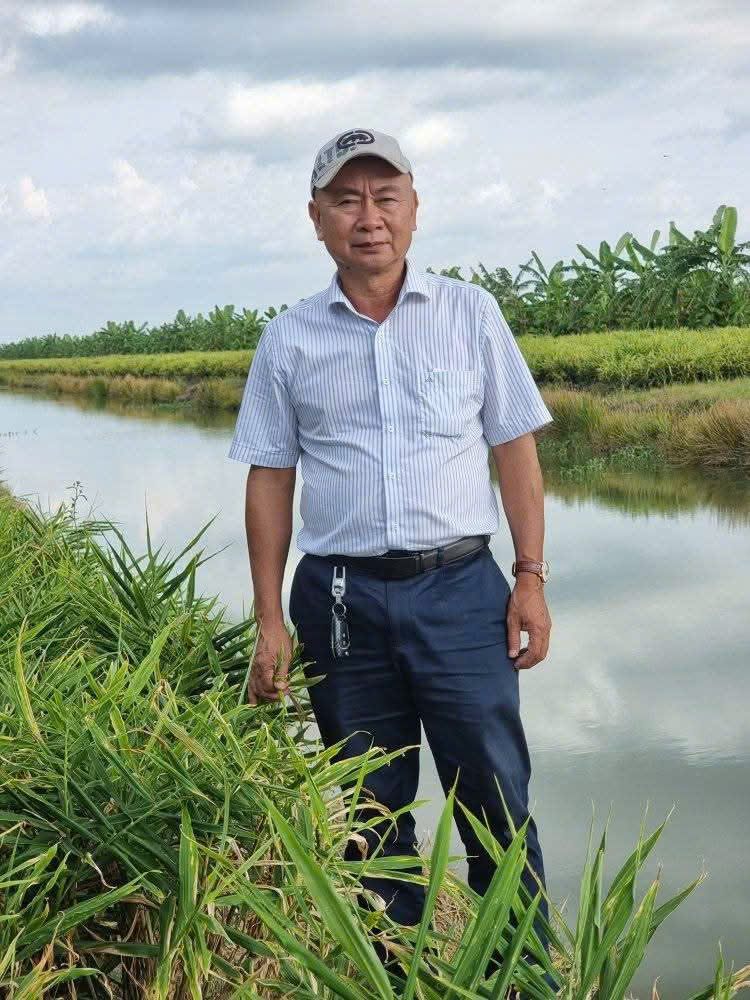 Anh Phan Khánh đứng bên bờ kênh, sau lưng là ruộng và vườn chuối